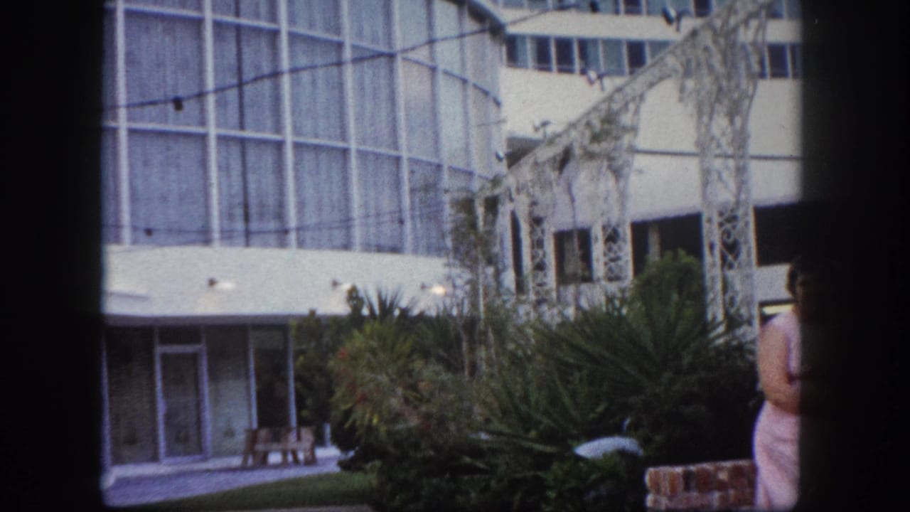 Mid-century modern glass curtain-wall building and white decorative pergola, likely Tampa Florida circa 1960; second woman in floral dress partially visible at frame right.
