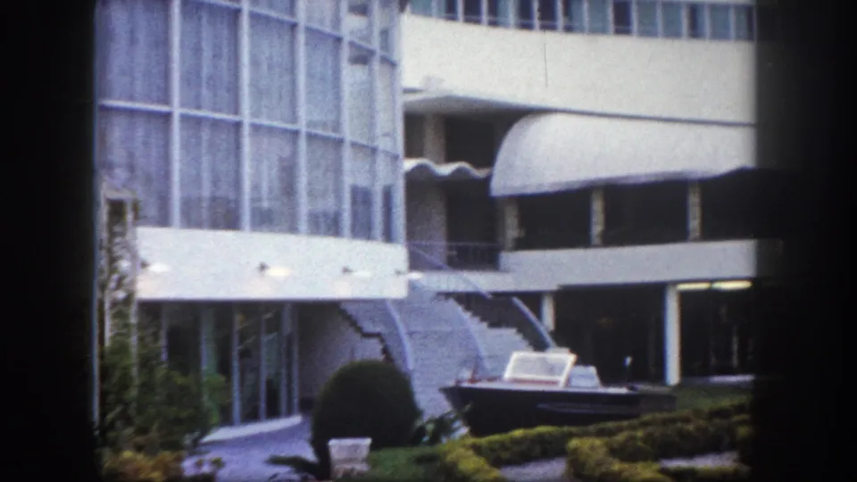 Modernist hotel facade in Tampa, Florida, circa 1960, with curved white canopies, geometric hedges, and a motorboat displayed in the courtyard.