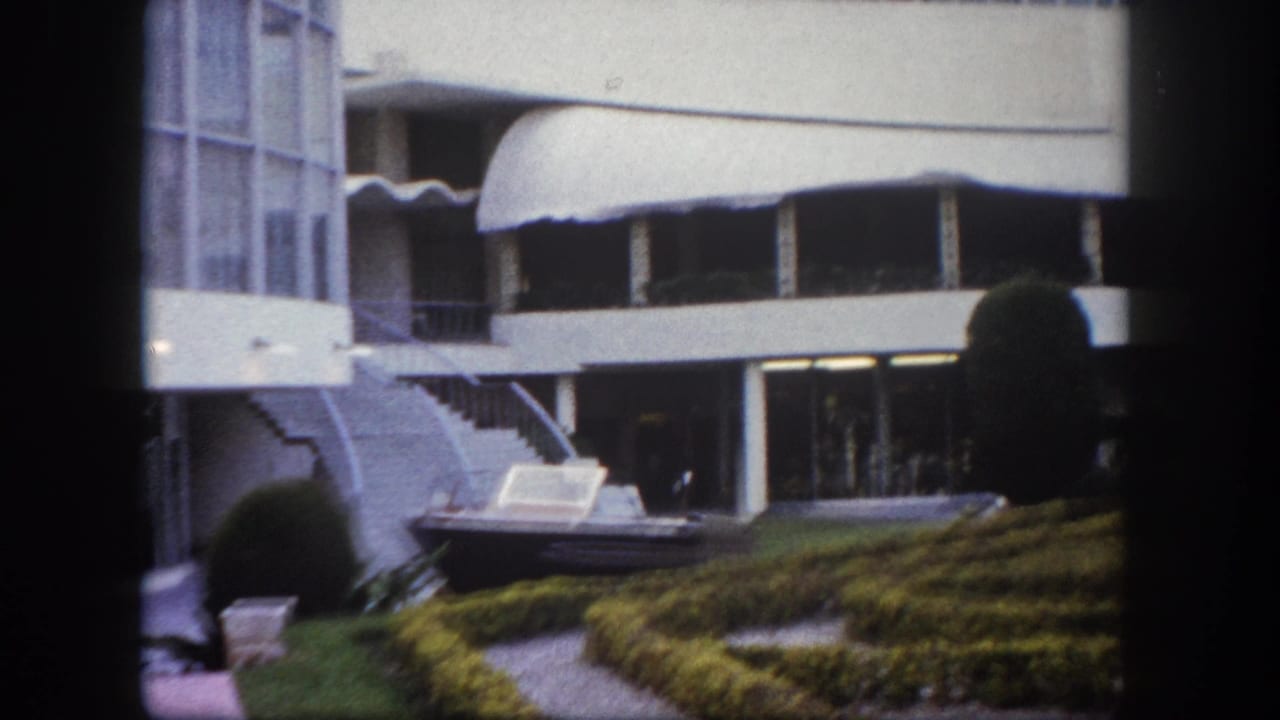 Hotel exterior pan in Tampa, Florida, circa 1960, showing curved concrete canopies, round topiary, and motorboat courtyard display.