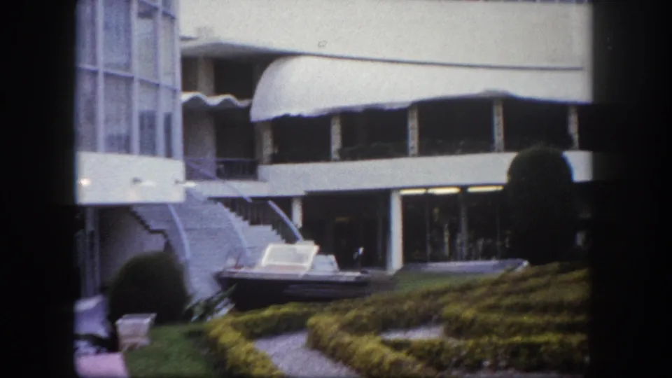 Hotel exterior pan in Tampa, Florida, circa 1960, showing curved concrete canopies, round topiary, and motorboat courtyard display.