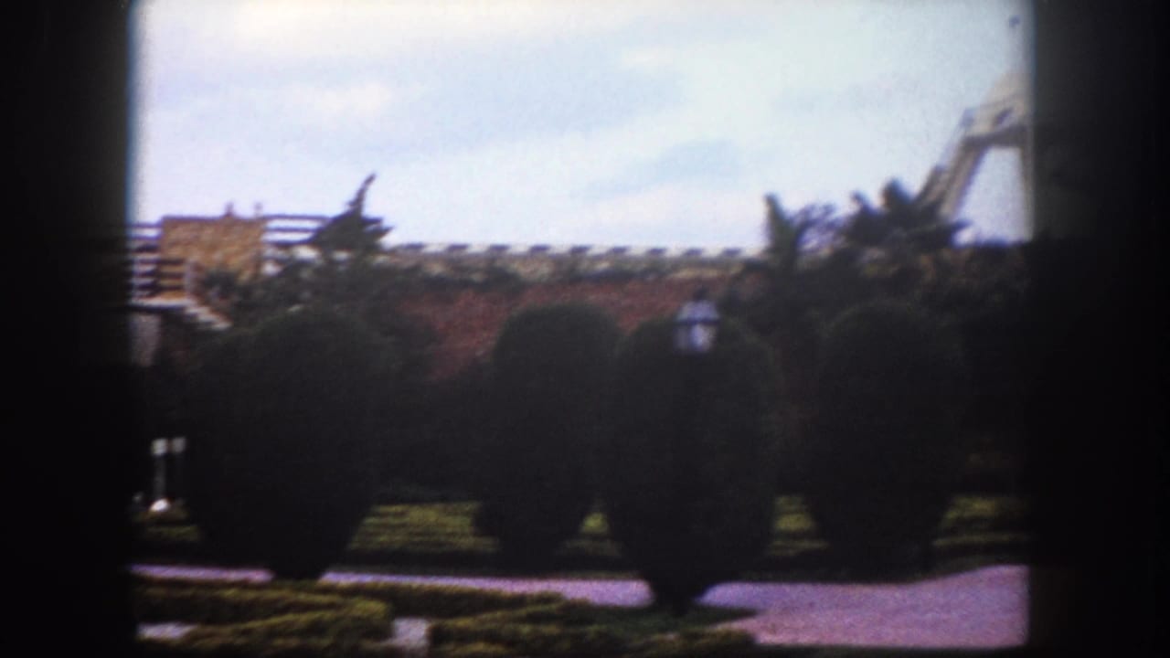 Public garden with spherical topiary shrubs; modernist building visible at left and a striped canopy structure emerging at right.