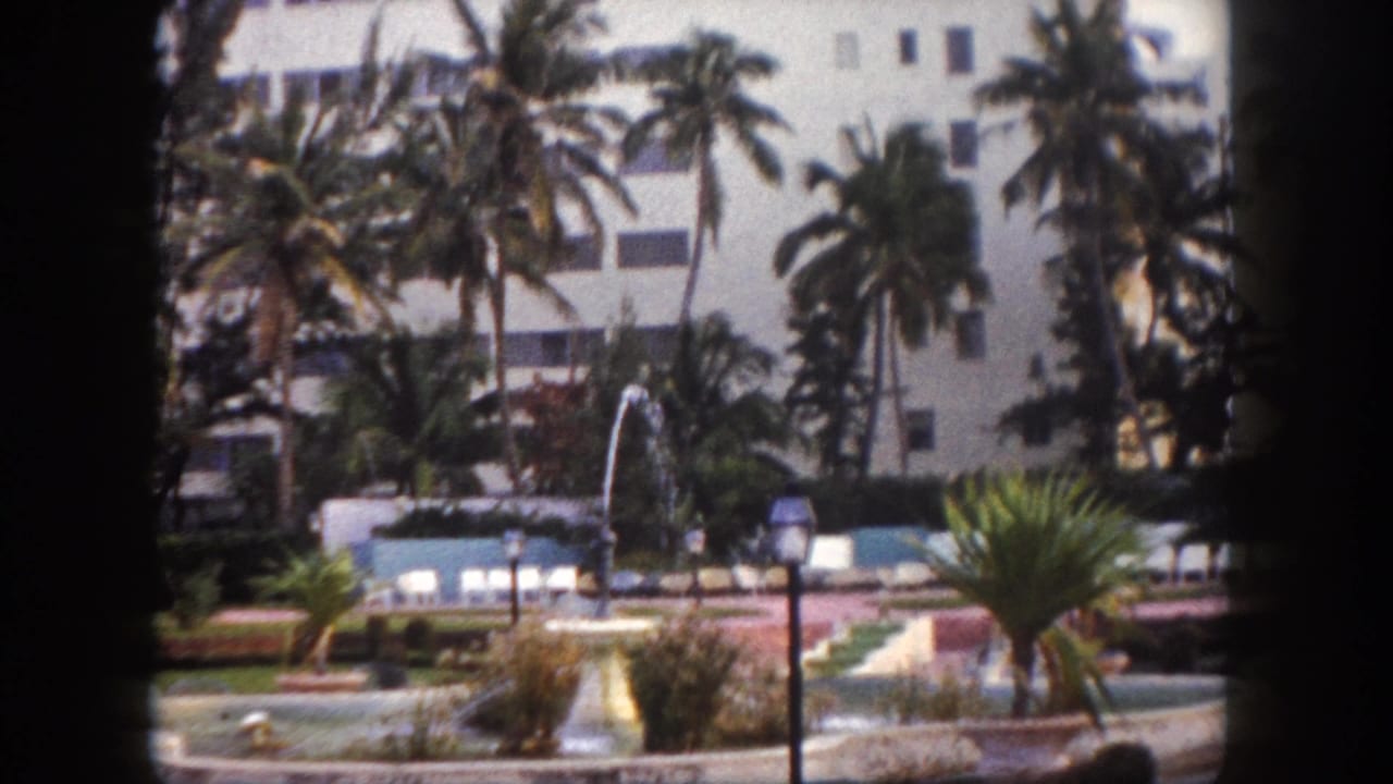 Poolside fountain garden at a Tampa, Florida resort circa 1960, with tall palm trees and a white modernist hotel building, shot on 8mm film.