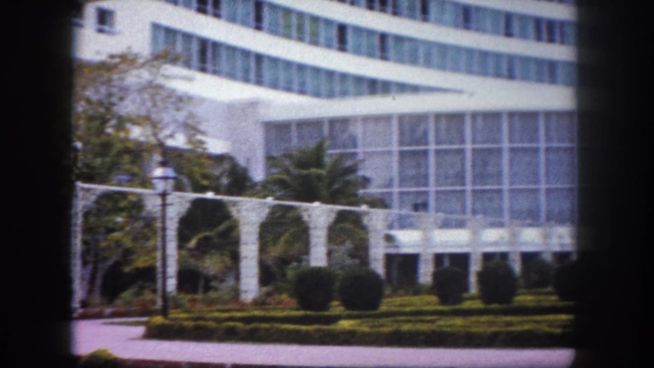 8mm film frame circa 1960, Tampa, Florida: large curved government building with formal garden, white decorative trellis, and a classic lamppost in the left foreground.