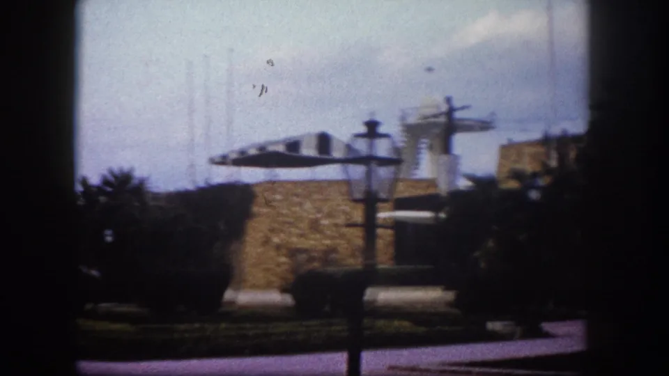 8mm home movie, c. 1960, Tampa, Florida: decorative lamppost beside a low stone masonry wall; a sculptural disc-shaped element and low outbuildings in the background over lawn.