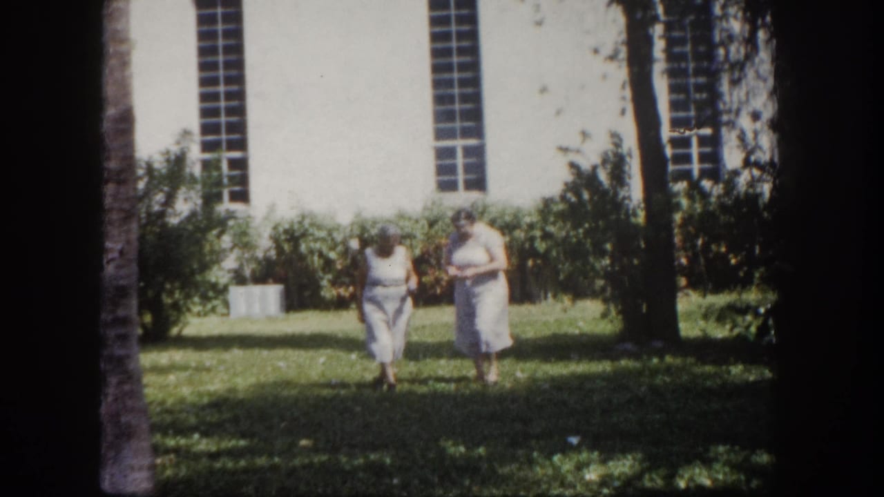 Two elderly women in light summer clothing advancing toward camera on a sunny lawn in front of a white stucco building, c.1960 Tampa, Florida.