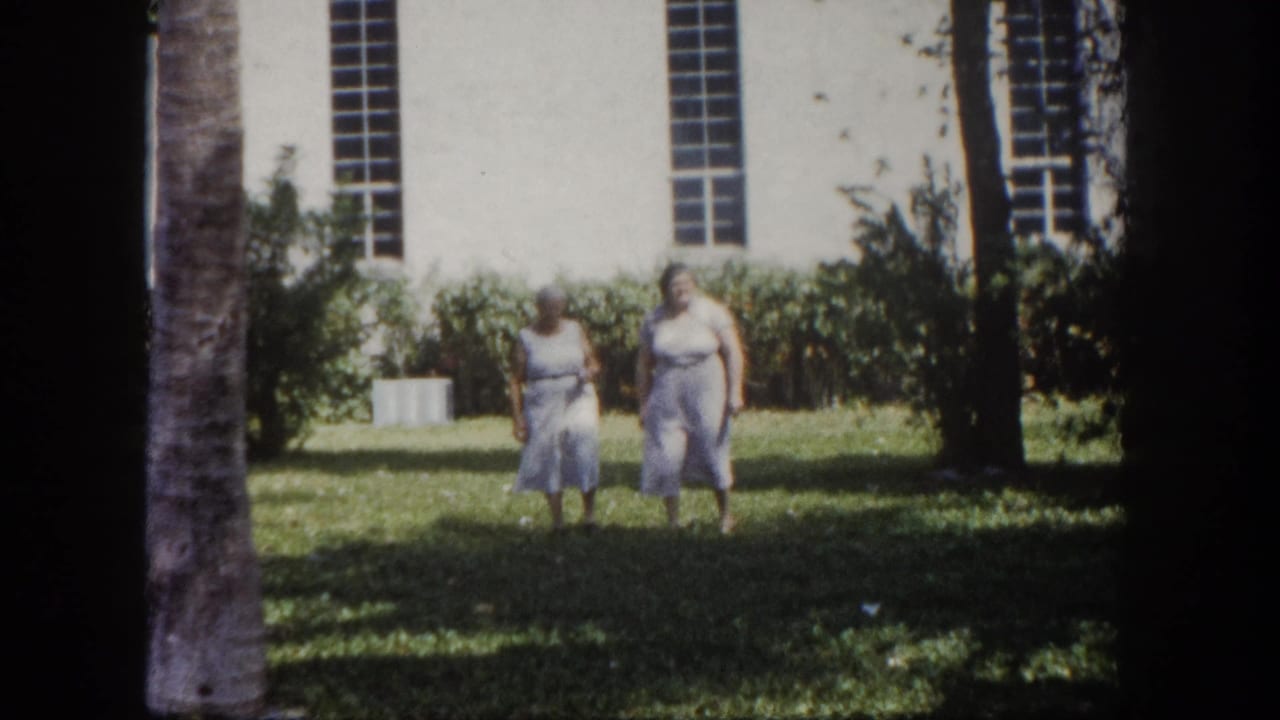Two adult women pause briefly on the lawn before a white institutional building with tall narrow windows, Tampa, Florida, circa 1960, 8mm film.