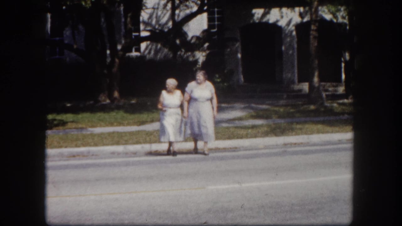 Two elderly women stand together at a Tampa, Florida roadside circa 1960, in light casual dresses on a sunny day — 8mm home movie footage.