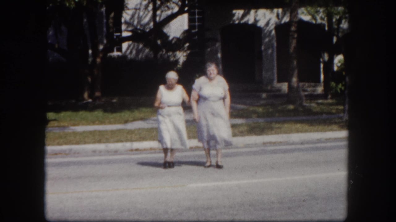 Two elderly women in early-1960s pale dresses cross a quiet residential street, likely Tampa, Florida, circa 1960, filmed on 8mm color stock.