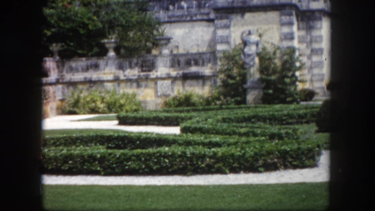 Geometric boxwood hedges and manicured lawn in a formal garden, with a stone building bearing classical statues, Tampa, Florida, circa 1960.