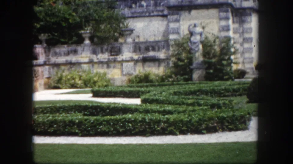 Geometric boxwood hedges and manicured lawn in a formal garden, with a stone building bearing classical statues, Tampa, Florida, circa 1960.