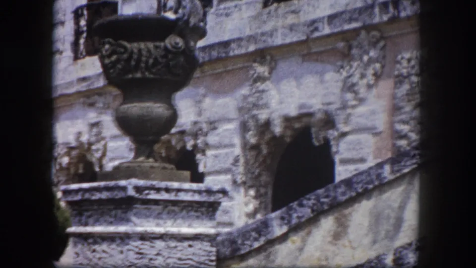 Ornate cast-metal urn with decorative relief on a stone pedestal against carved stone building wall, Tampa, Florida, circa 1960.