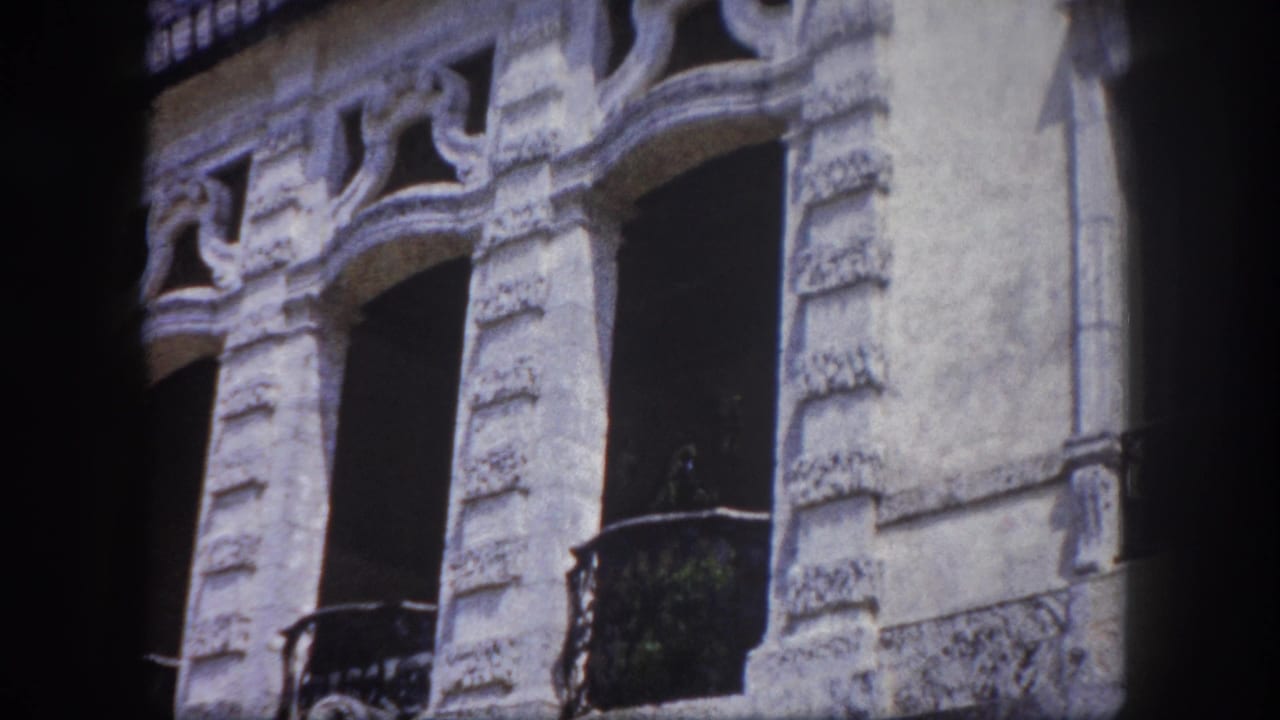 Multi-story ornate stone building facade with arched windows, carved decorative surrounds, and wrought iron balconies; 8mm home movie footage from Tampa, Florida, circa 1960.