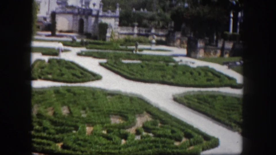 Formal garden maze with geometric hedge patterns and winding paths viewed from visitor's vantage; white estate building in background, Florida, c. 1960.