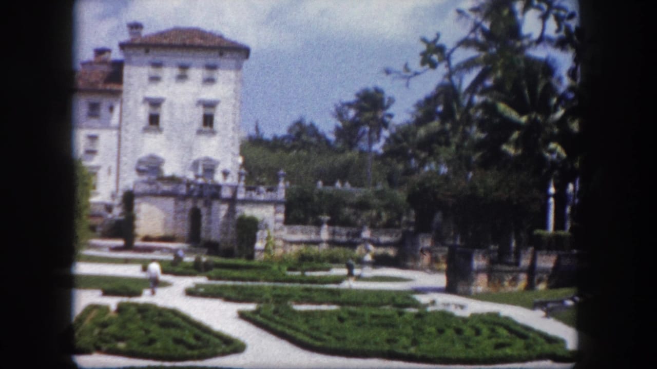 Grand white estate building with cylindrical tower and terracotta roof viewed across geometric garden, with decorative garden sphere and palm trees, Florida, c. 1960.