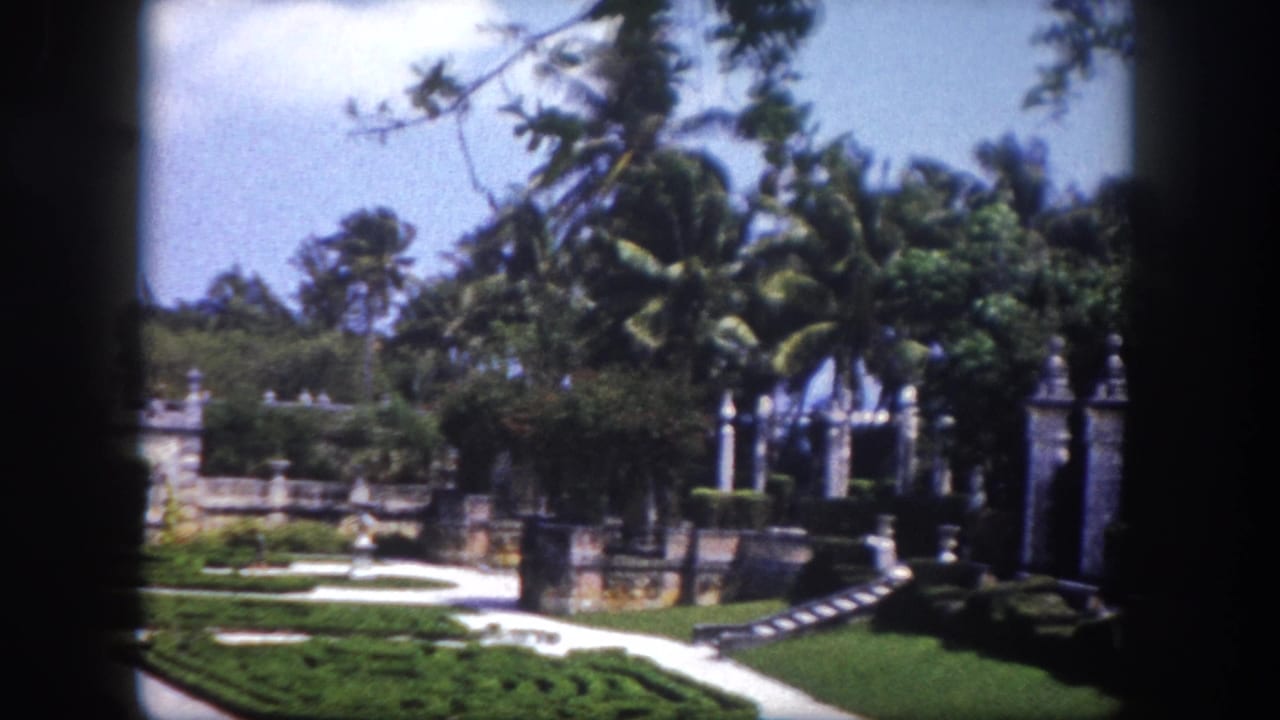 8mm home movie frame showing a formal parterre garden with ornate stone gate pillars and tall palms, Tampa, Florida, circa 1960.