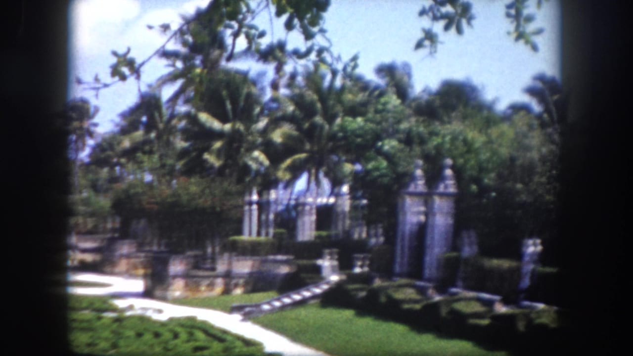 8mm home movie frame of ornate stone garden gate and formal hedged parterre with palms and blue sky, Tampa, Florida, circa 1960.