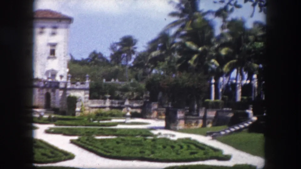 8mm home movie frame revealing a Mediterranean-style building with tiled roof beside a formal parterre garden and stone gate pillars, Tampa, Florida, circa 1960.