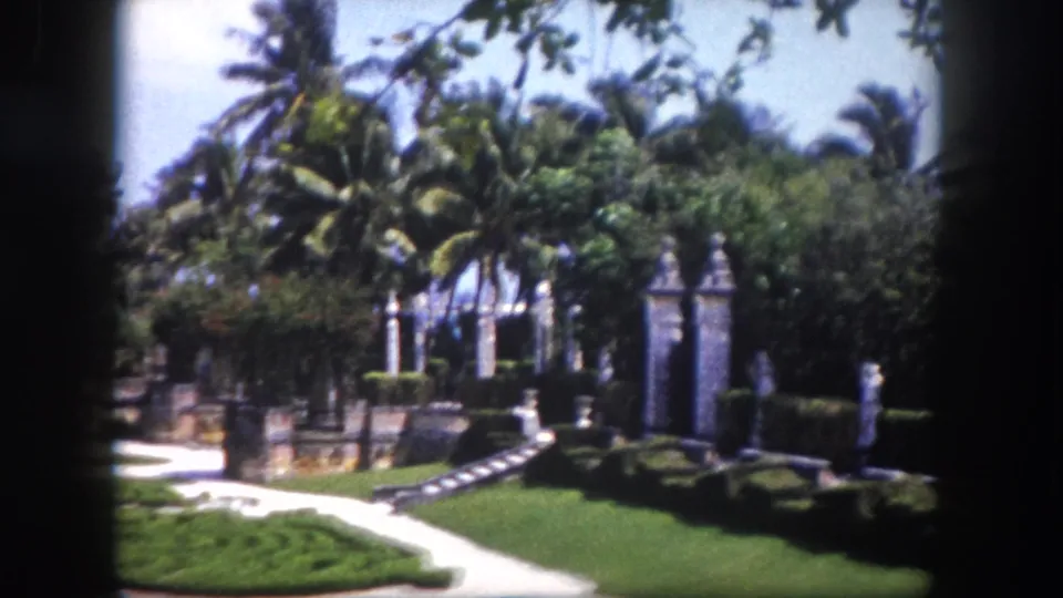 8mm home movie wide view of a formal parterre garden with ornate stone gate pillars and tall palms, Tampa, Florida, circa 1960.