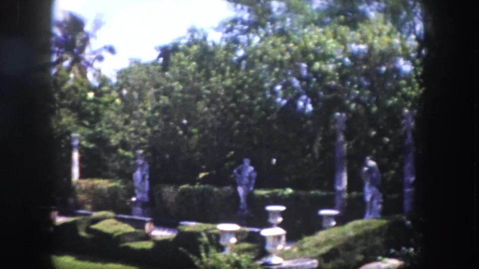Stone figurative statues on pedestals and decorative urns in a formal Florida ornamental garden with dense tropical canopy, circa 1960, 8mm film.