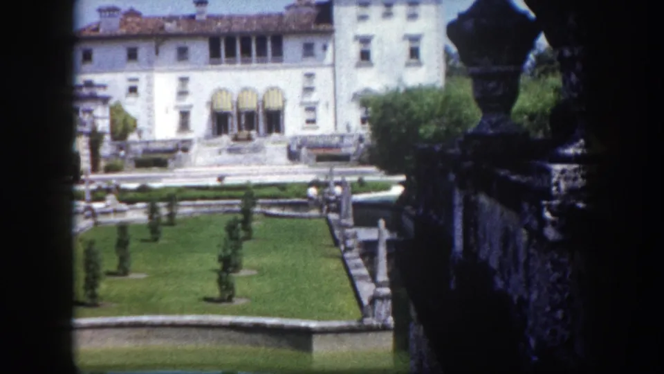White classical mansion facade with symmetrical topiary gardens, reflecting pools, and a stone urn finial in the foreground, Tampa, Florida, circa 1960.