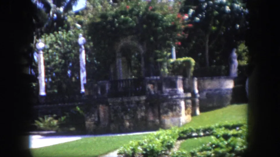 8mm film circa 1960, formal garden terrace with classical columns and stone wall at a Florida estate, camera mid-pan.