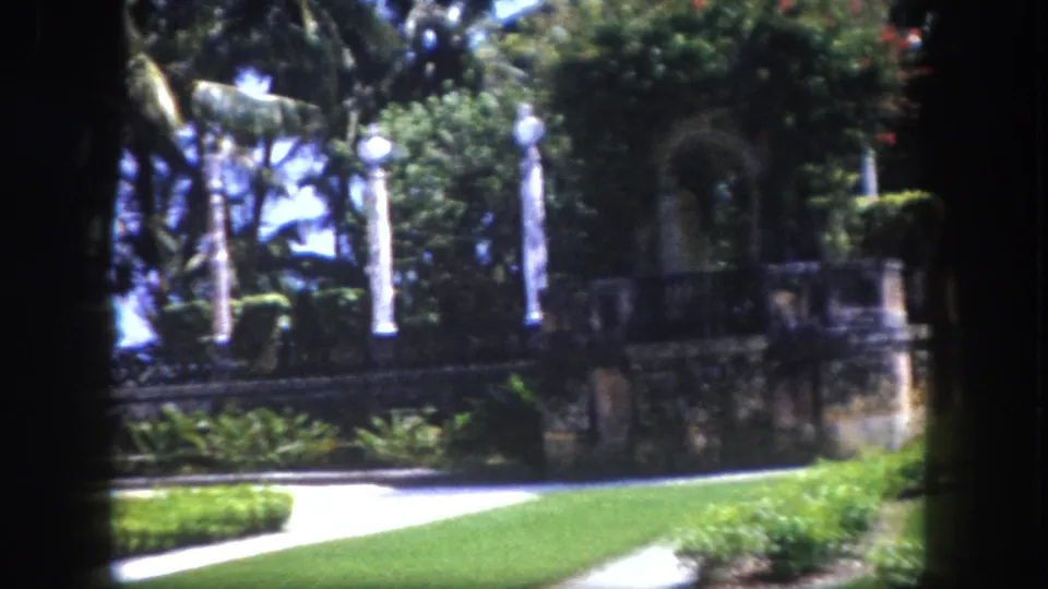 8mm home movie circa 1960, formal garden colonnade with palm trees and stone balustrade at a Florida estate, late in the pan sequence.