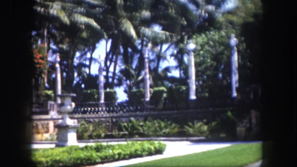 Final 8mm frame circa 1960 of a Florida estate garden, ornamental colonnade and palms as the slow camera pan concludes.