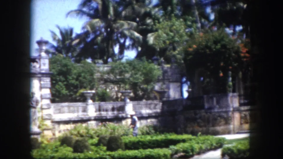 8mm film circa 1960, Tampa, Florida: figure in light clothing at lower left, stone balustrade and manicured hedges in foreground, tall palms behind.