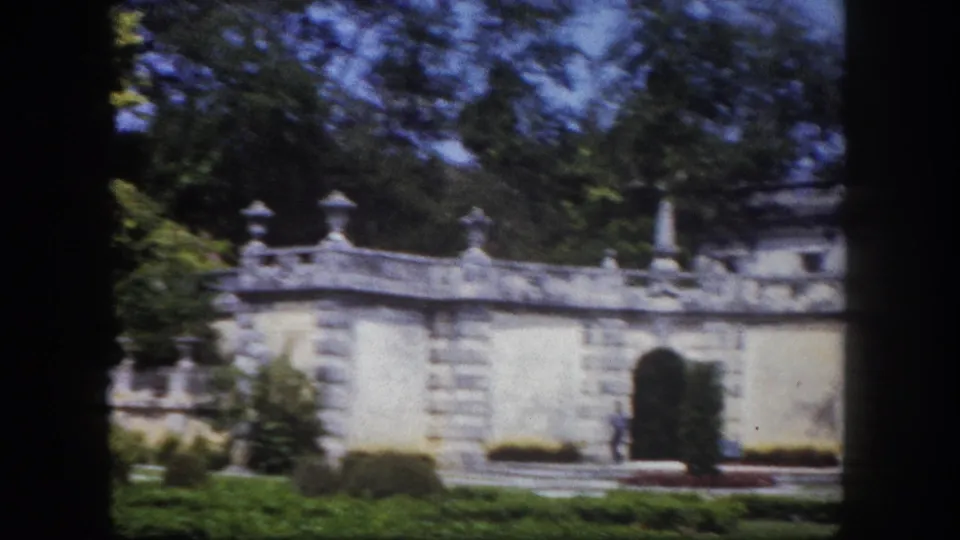 8mm film frame circa 1960 showing ornate stone garden walls with decorative finials and stone urns in a formal Florida estate garden, dense trees framing the composition.