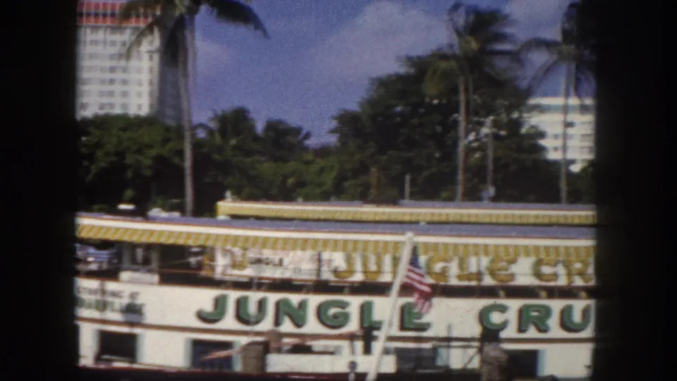 Jungle Cruise boat at Tampa, Florida waterfront, circa 1960 — white hull with bold green lettering, American flag, and yellow awning trim; 8mm film.
