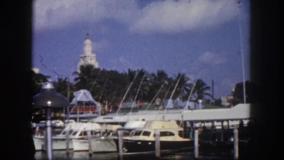 Tampa waterfront marina, circa 1960 — motorboats and cruisers docked at pier, palm trees, and a tower structure visible in background; 8mm film.