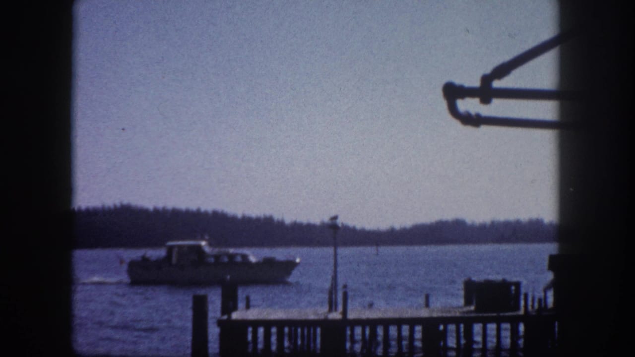 Motorboat on open bay water with wooden dock pilings, shot through a window frame, early 1960s Tampa Florida waterfront, 8mm film.