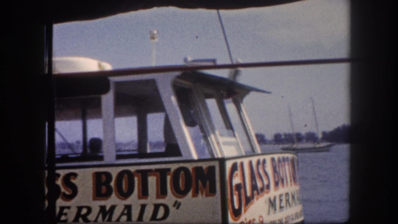 Upper section and name signage of the 'Glass Bottom Boat Mermaid' tour vessel at a Florida marina, circa 1960, shot through a window frame.