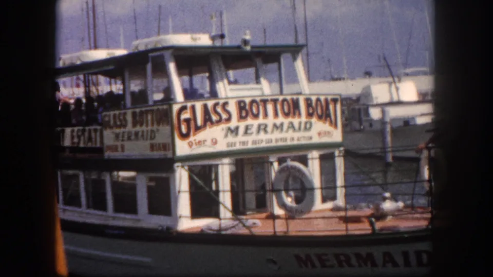 'Glass Bottom Boat Mermaid, Pier 9 - See the Deep-Sea Diver in Action' tour vessel at a Florida marina, circa 1960, with moored boats in background.