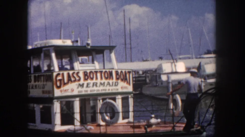 'Glass Bottom Boat Mermaid' tour vessel at Pier 9, Florida marina, circa 1960, with other vessels moored alongside, viewed through window frame.