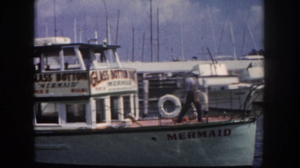 Glass Bottom Mermaid tourist vessel at Pier 9, Miami, circa 1960, crew member walking the deck with marina masts in background, shot on 8mm color film.