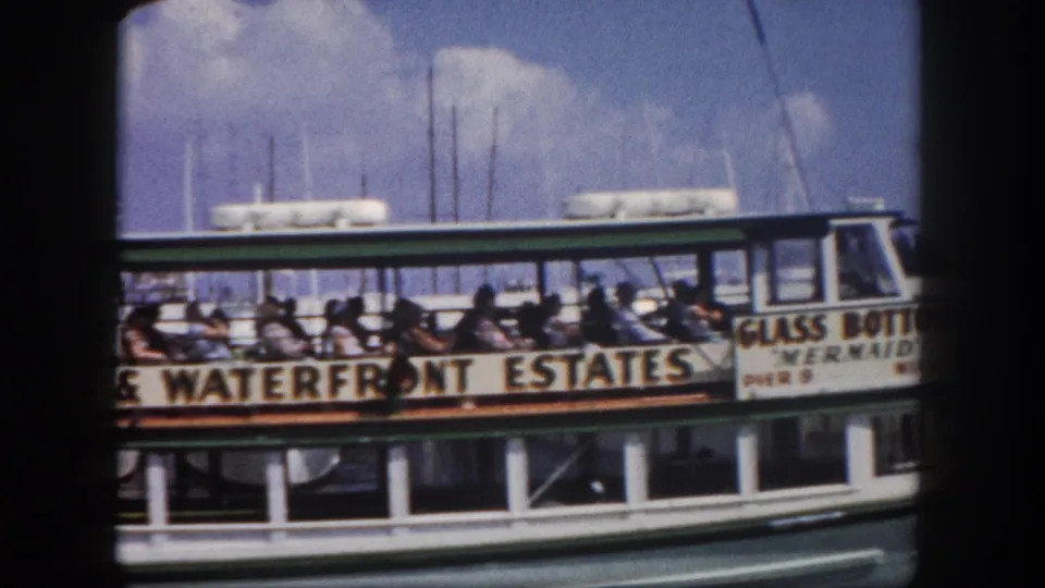 Passengers seated on the open-air deck of the Glass Bottom Mermaid tourist boat, Miami, circa 1960; Waterfront Estates advertising banner visible along the lower hull.