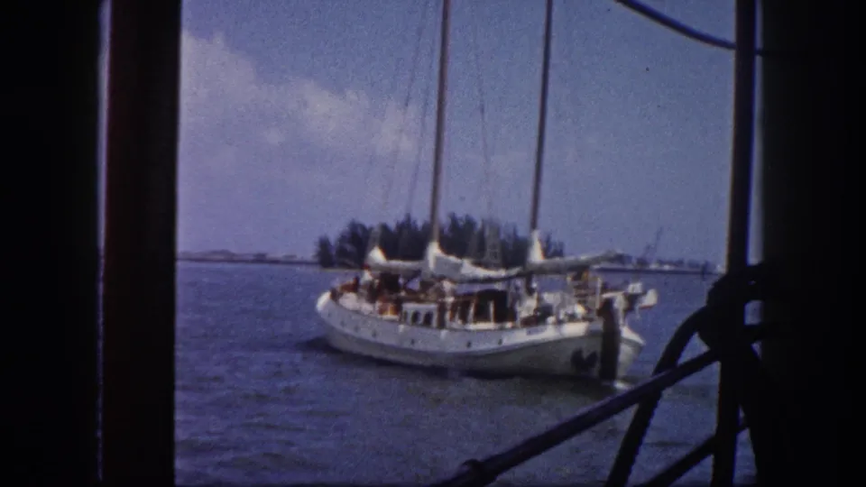 Sailboat underway on a Florida waterway, shot handheld from a moving vessel with foreground rigging; c.1960 8mm, consistent with the marina context of adjacent frames.
