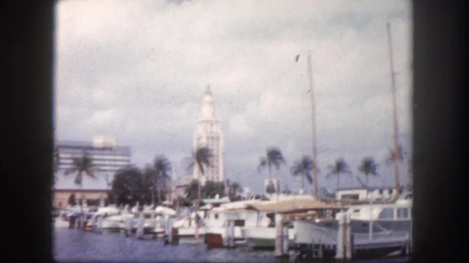1960s Florida marina with docked boats and a white Mediterranean-style spired tower building in the background — location may be Miami waterfront, c.1960.