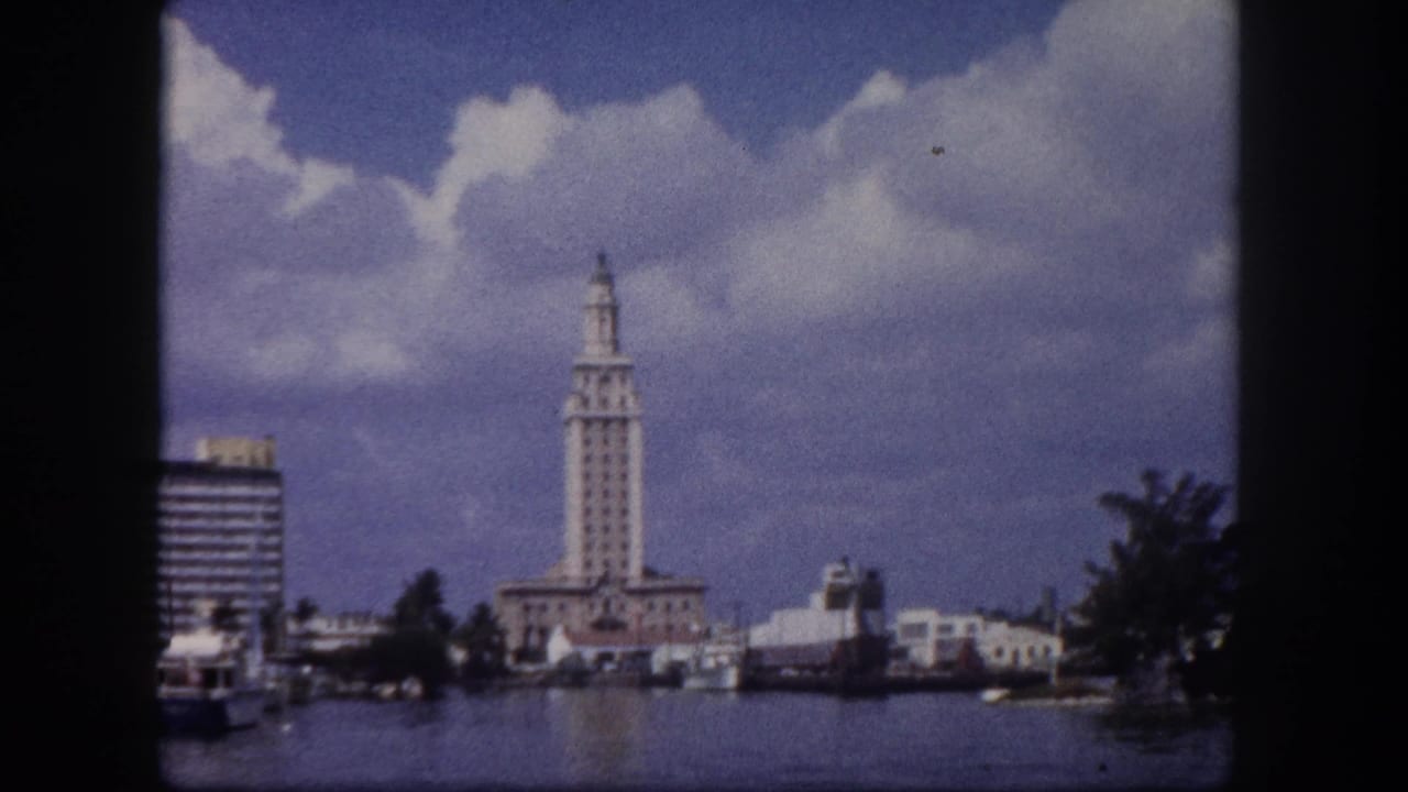 8mm harbor scene circa 1960 showing a distinctive ornate tower and mid-century waterfront buildings along a Florida waterway under cumulus clouds.