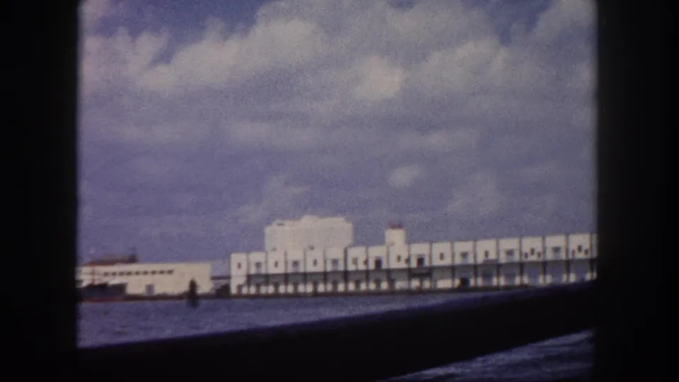 8mm harbor view circa 1960 showing a white colonnaded pier at the water's edge under large cumulus clouds, Florida.