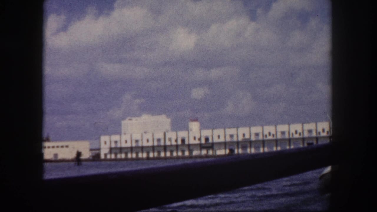 View from a moving boat of a long white multi-bay dock building along a harbor waterfront.