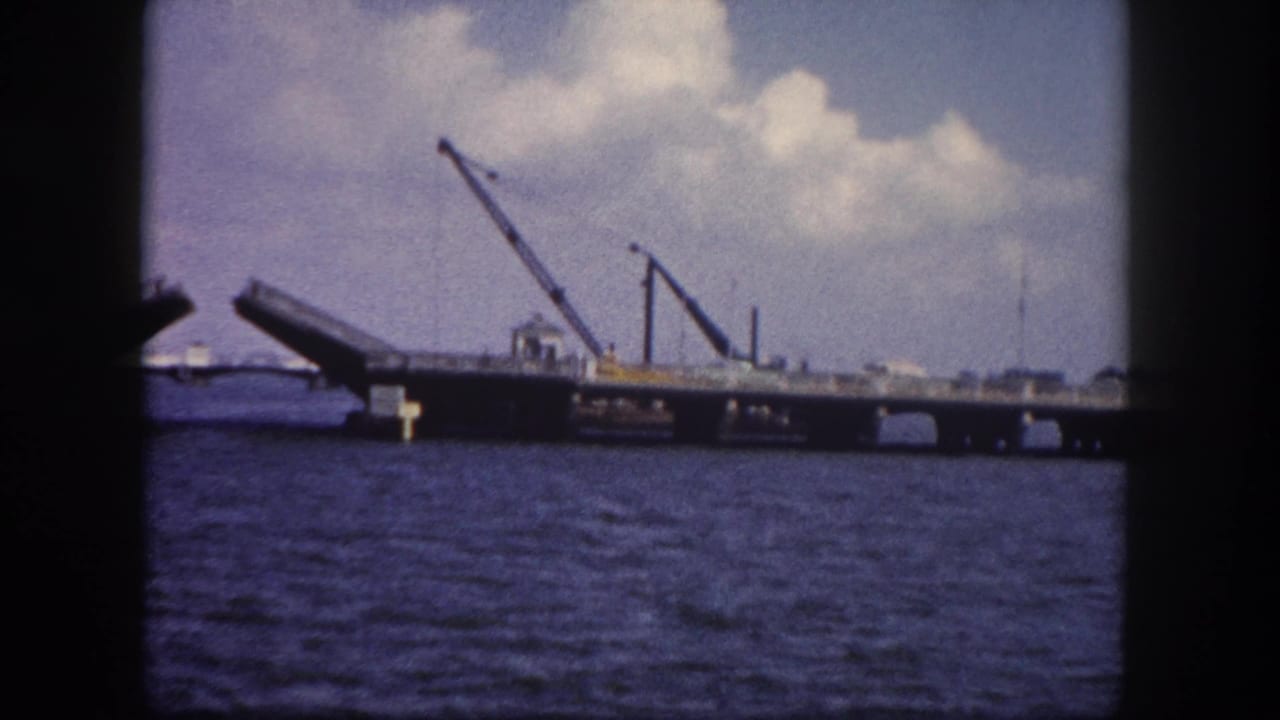 Early-stage drawbridge opening on a Tampa, Florida waterway circa 1960, with two cranes on the bridge deck and choppy blue harbor water below.