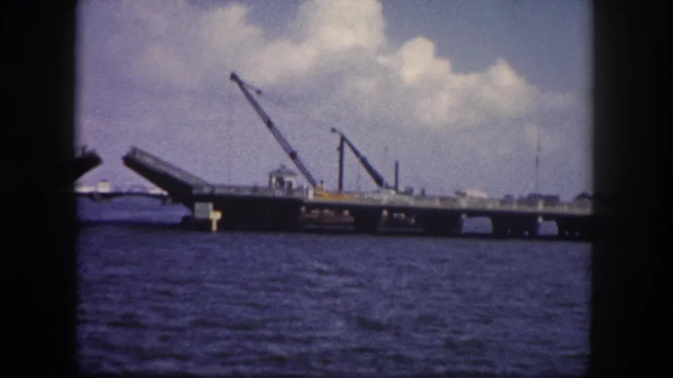Early-stage drawbridge opening on a Tampa, Florida waterway circa 1960, with two cranes on the bridge deck and choppy blue harbor water below.