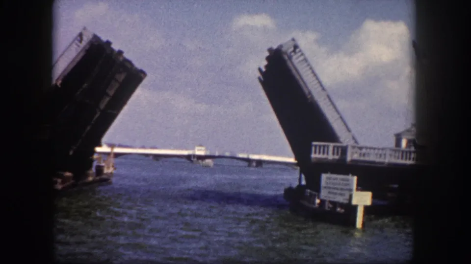 Drawbridge fully open on Tampa, Florida waterway circa 1960; bascule leaves raised steeply, bridge control booth and a small sign visible at water level.