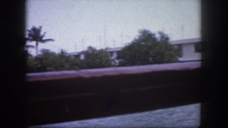 8mm home-movie frame circa 1960, Tampa Florida — flat-roofed waterfront structure and palm trees viewed from a moving boat with railings in foreground.