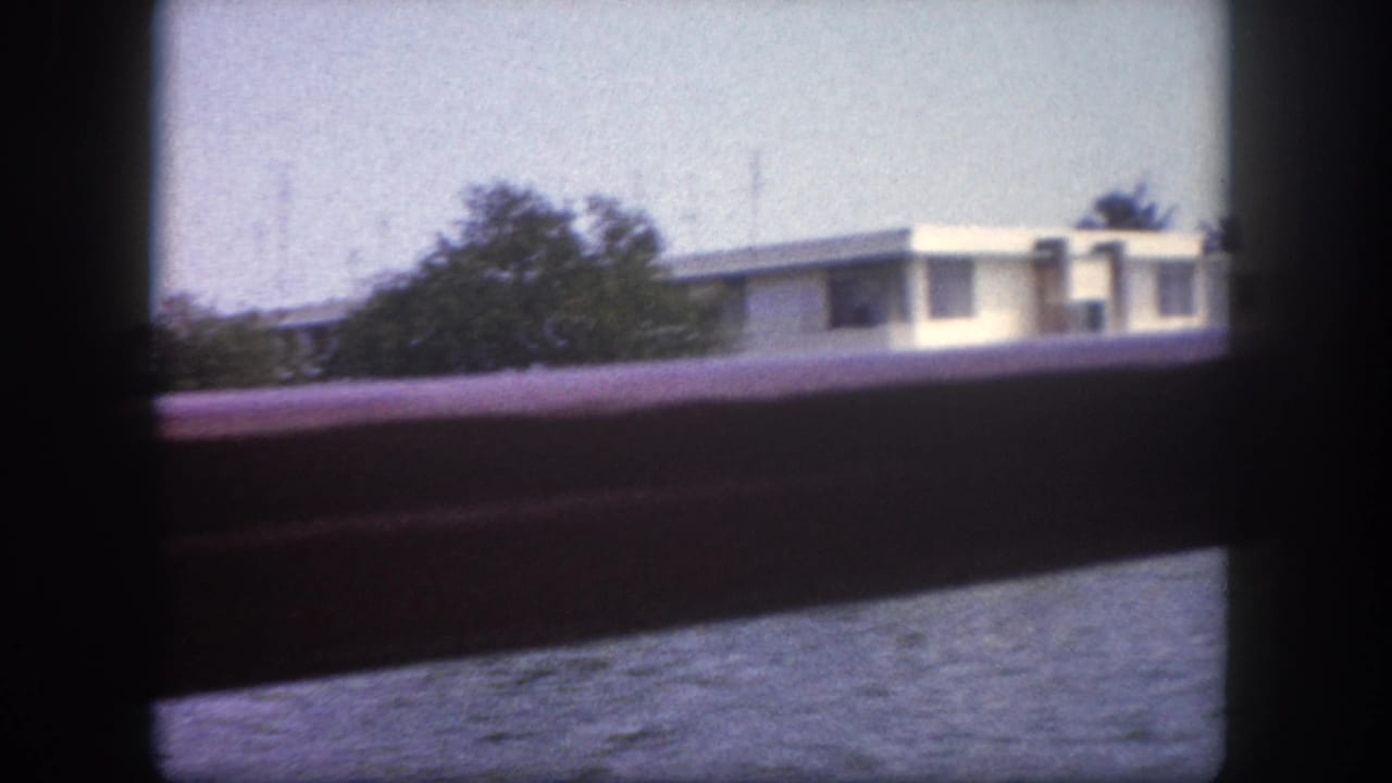 8mm home movie frame from Tampa, Florida, circa 1960: flat-roofed white building seen across water through a boat railing.