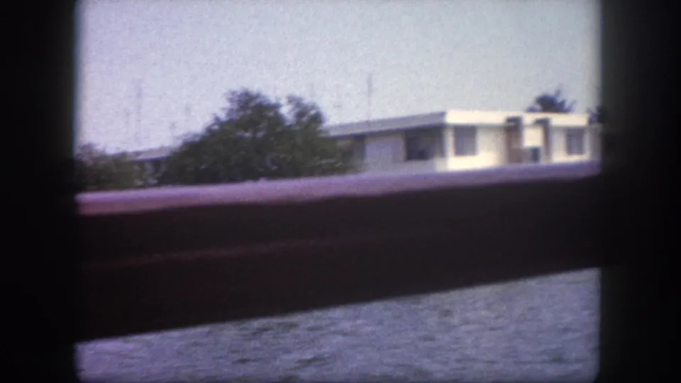 8mm home movie frame from Tampa, Florida, circa 1960: flat-roofed white building seen across water through a boat railing.