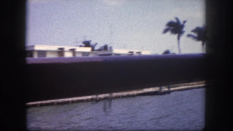 8mm home movie frame from Tampa, Florida, circa 1960: waterfront building with dock and palm tree visible through railing from a moving boat.