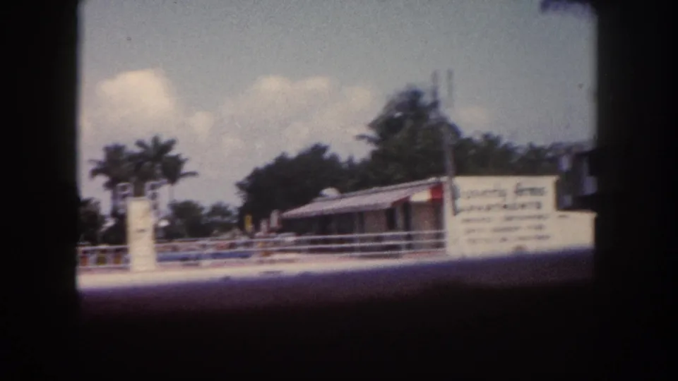 White waterfront commercial building with partially legible signage, palm trees, and dark 8mm border framing; Tampa, Florida, circa 1960.